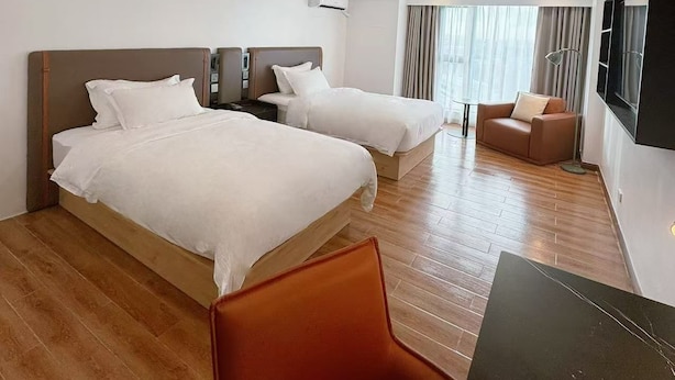 A hotel room with two beds, a sofa, a TV, and a wooden floor.