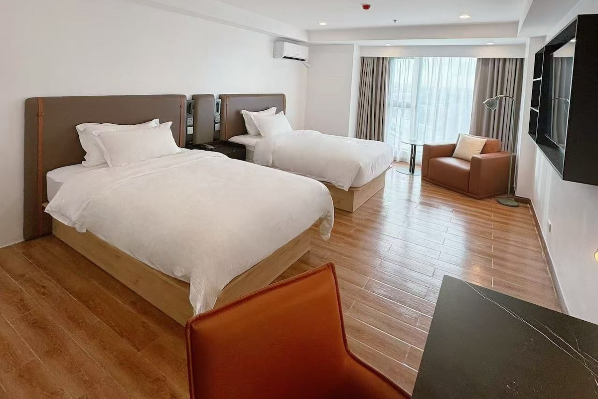 Habitación de hotel con dos camas, un sofá, un televisor y piso de madera.