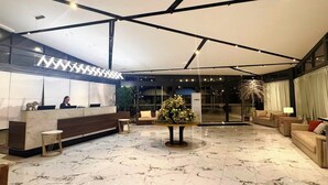 A hotel lobby with a reception desk, seating area, and a large plant centerpiece.