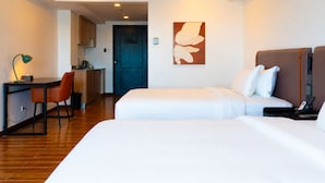 A hotel room with two beds, a desk, a chair, a painting, and a door.