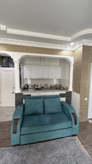 A living room with a teal sofa, a kitchen area with white cabinets, and a decorative wall. - Umid 2026 Hotel (Batumi)
