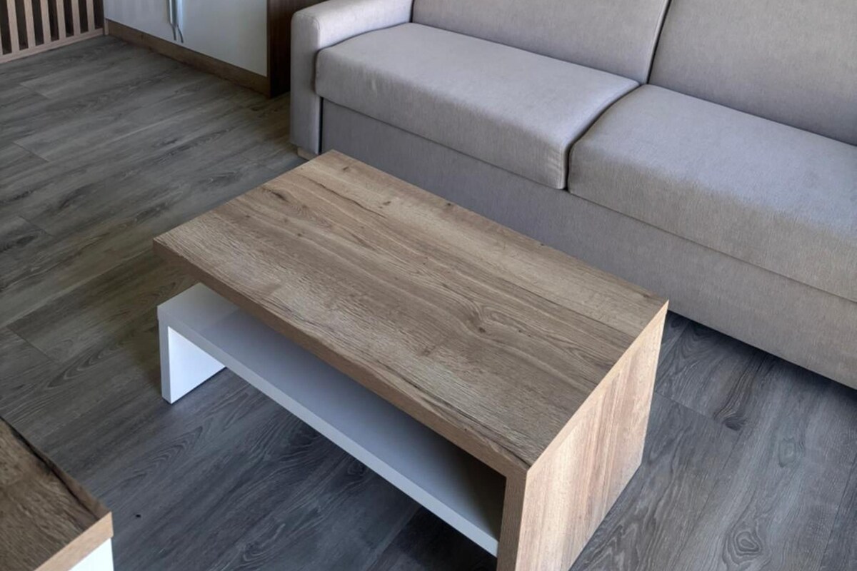 Una sala moderna con un sofá gris, una mesa de centro de madera y piso de madera.
