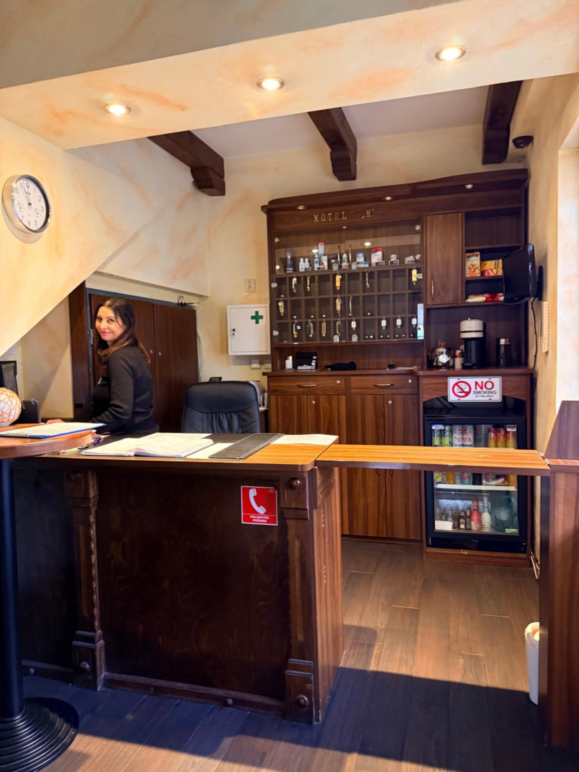 A reception desk with a 'No Smoking' sign, a clock, and a 'Call Emergency' sign.