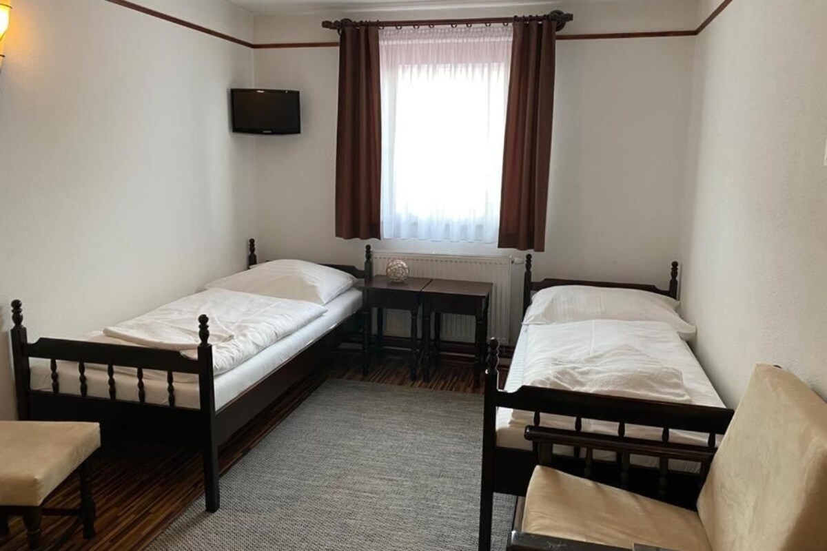 Una habitación con dos camas individuales, una mesita, una silla y un televisor montado en la pared.