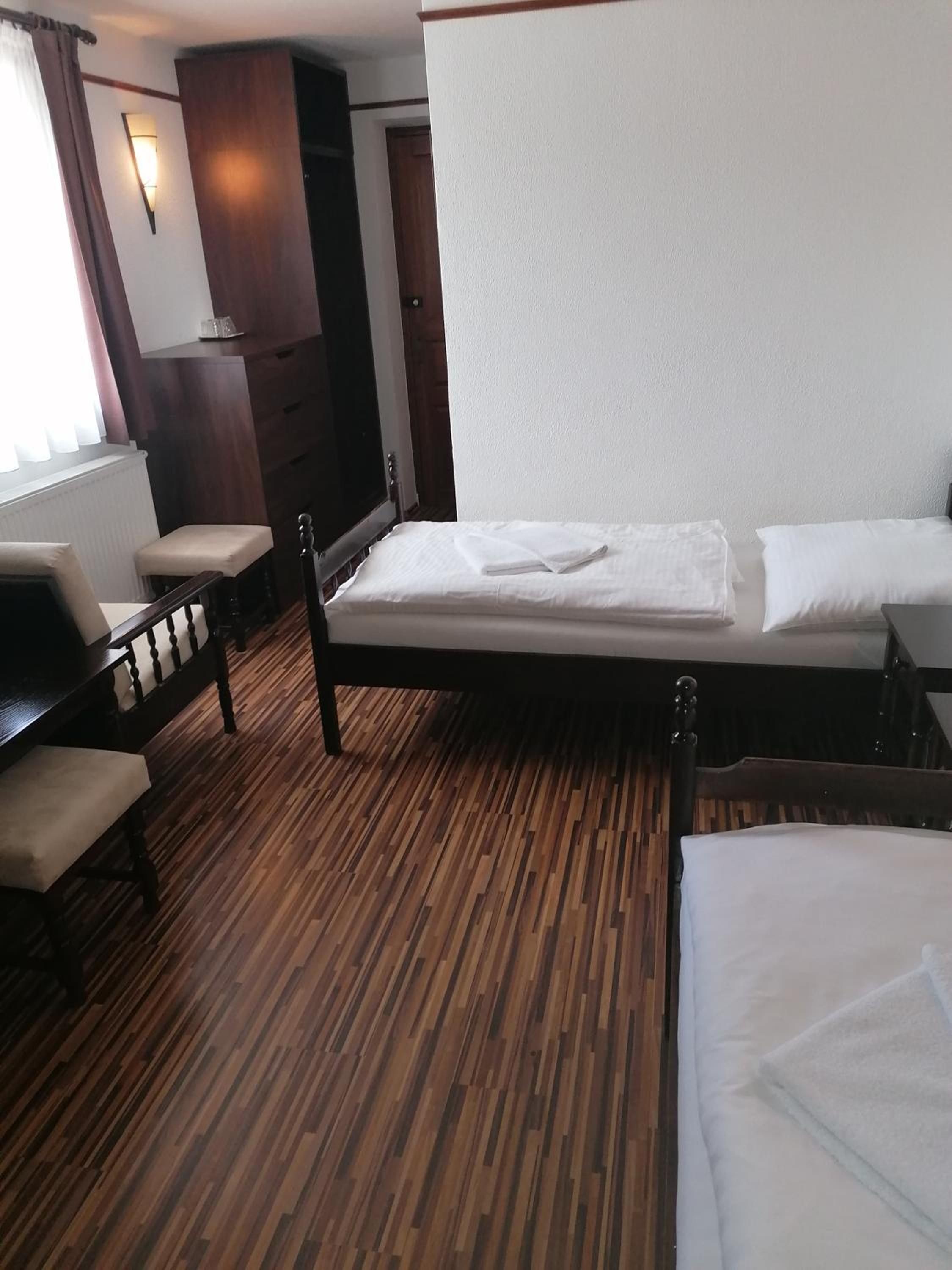 Una habitación de hotel con piso de madera, una cama con ropa blanca, un banco de madera y una lámpara de pared.