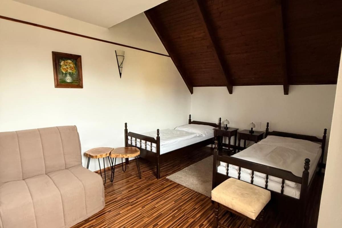 A compact room with a wooden floor, a sofa, a bed, a small table, and a painting on the wall.