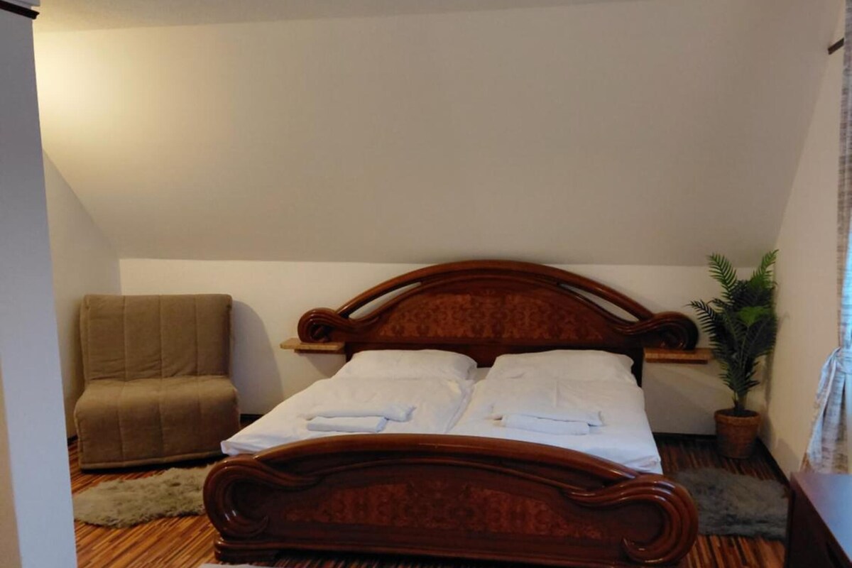 Un dormitorio con cama de madera, una silla, una planta en maceta y suelo de madera.