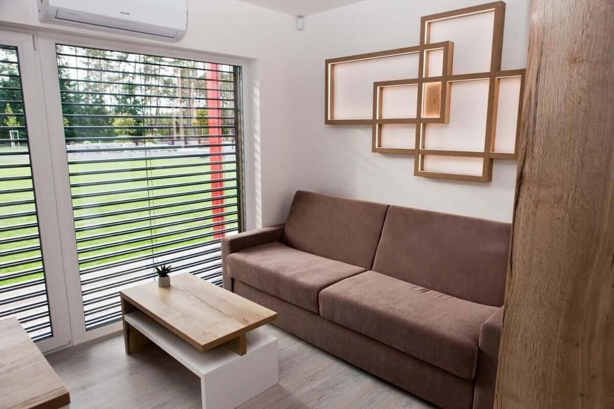 Una sala moderna con un sofá marrón, una mesa de centro de madera y un aplique de pared.