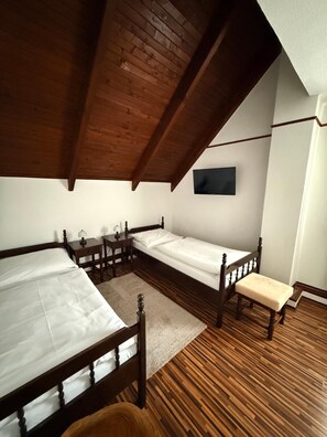 Una habitación con dos camas de madera, un banco, una mesita con lámparas y un televisor de pantalla plana montado en la pared.