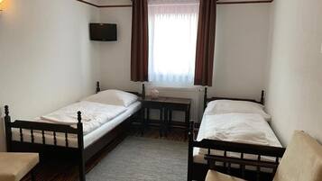 Una habitación con dos camas individuales, una mesita, una silla y un televisor montado en la pared.