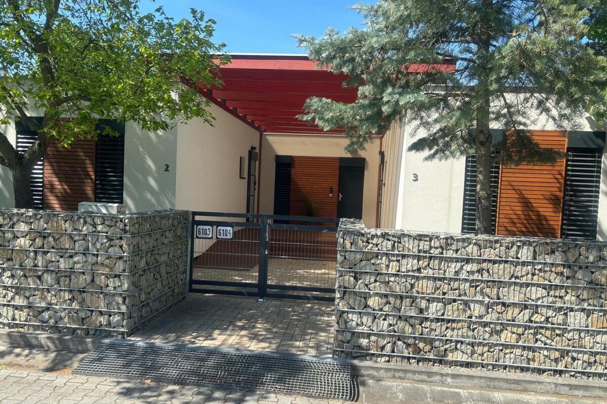 A gated entrance with a stone wall, a metal gate, and a red-roofed building with numbered doors.