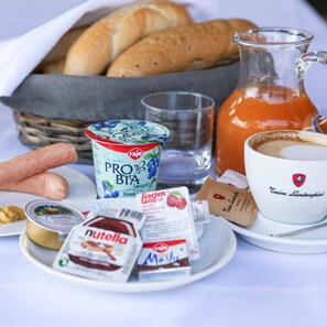 Un desayuno con pan, una jarra de zumo de naranja, una taza de café y diferentes salsas y condimentos.