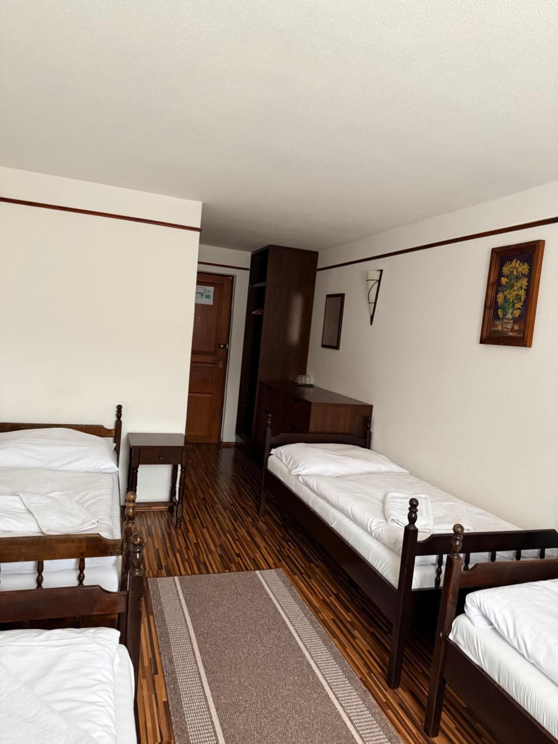 Una habitación con dos camas de madera, un armario de madera, una mesita y una puerta que da a otra habitación.