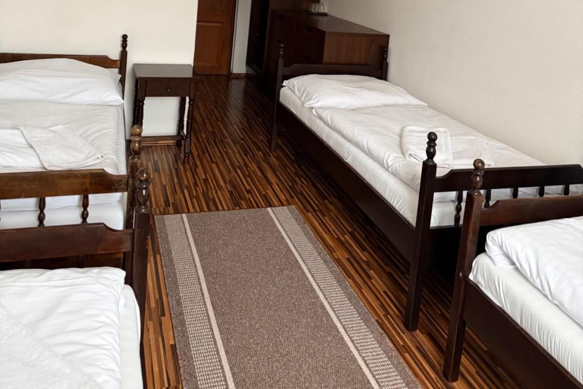 Een kamer met twee houten bedden, een houten kledingkast, een tafeltje en een deur naar een andere kamer.