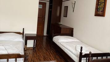 Una habitación con dos camas de madera, un armario de madera, una mesita y una puerta que da a otra habitación.