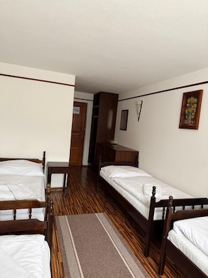 Een kamer met twee houten bedden, een houten kledingkast, een tafeltje en een deur naar een andere kamer.