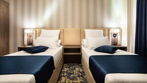 A hotel room with two single beds, a wooden headboard, bedside lamps, and a patterned carpet.