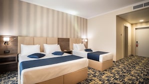 A hotel room with two beds, a wooden headboard, a patterned carpet, and a door leading to another room.