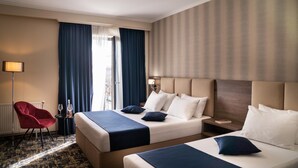 A hotel room with two beds, a red chair, a nightstand, and a window with curtains.