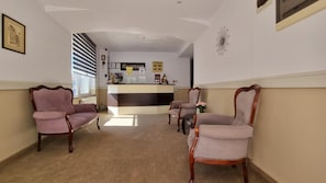 A reception area with a reception desk, framed pictures on the walls, and two upholstered chairs.