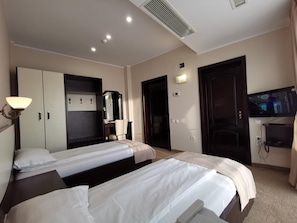 A hotel room with two beds, a desk, a mirror, a TV, and a wardrobe.