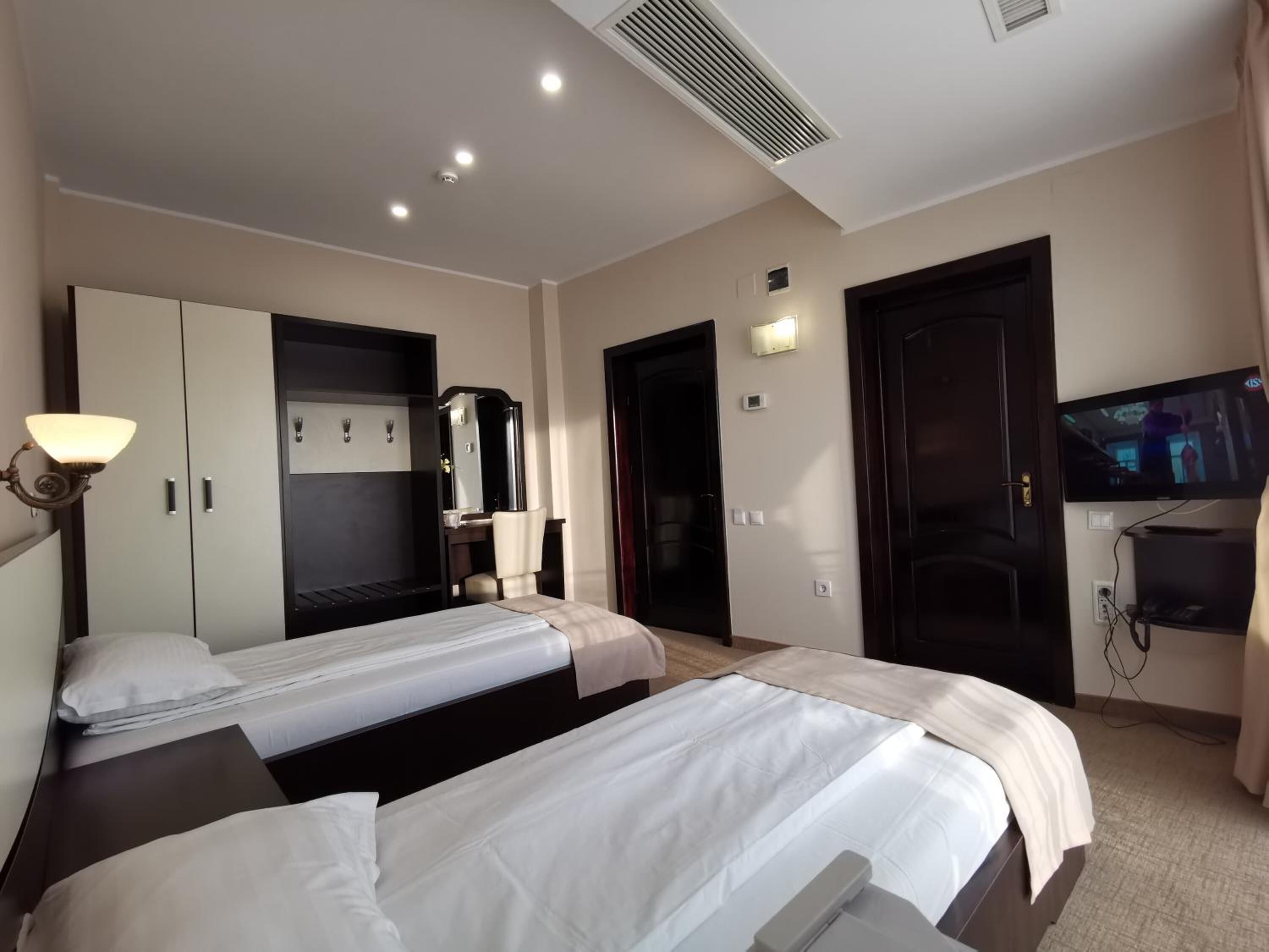 Habitación de hotel con dos camas, un escritorio, un espejo, un televisor y un armario.