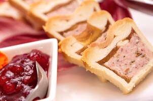 Uma fatia de torta de carne com crosta, acompanhada de molho de cranberry.