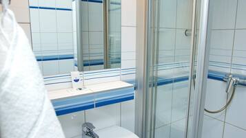 A bathroom with a glass shower enclosure, a sink with a mirror, and tiled walls.