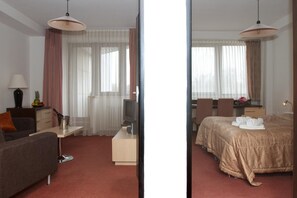Et hotelværelse med en seng, et skrivebord med lampe, et fjernsyn og en stol.