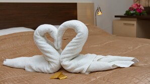 Una cama con un edredón marrón, una toalla blanca dispuesta en forma de corazón y un objeto dorado sobre la cama.