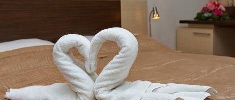 A bed with a brown quilt, a white towel arranged in a heart shape, and a gold object on the bed.