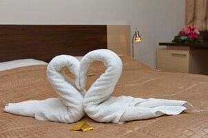 Uma cama com um edredom marrom, uma toalha branca dobrada em formato de coração e um objeto dourado sobre a cama.