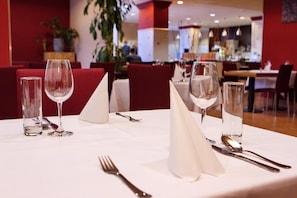 En restaurantscene med borde dækket til spisning, inklusiv vinglas, bestik og servietter.