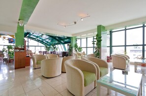 A spacious lobby with multiple seating areas, a glass coffee table, and large windows offering views. - Green Center Gili (Gostivar)