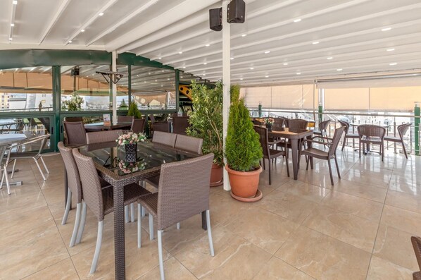 An indoor dining area with wicker furniture, a glass-top table, and potted plants.