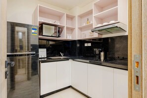 A modern kitchen with a black refrigerator, a microwave, and a stove. There are white cabinets and a black countertop. - Brassbell L Zamalek L Chroma L Central Location (Cairo)