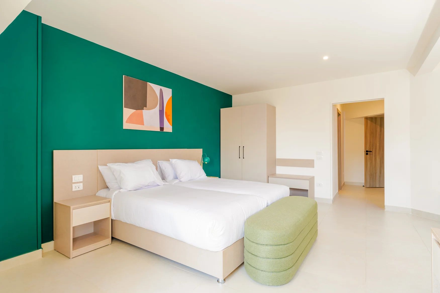 A modern bedroom with a bed, bedside tables, a green wall, and a door leading to another room.