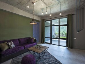 Un saló modern amb un sofà morat, una taula de centre de fusta i una gran porta corredissa de vidre que dona a una zona exterior.