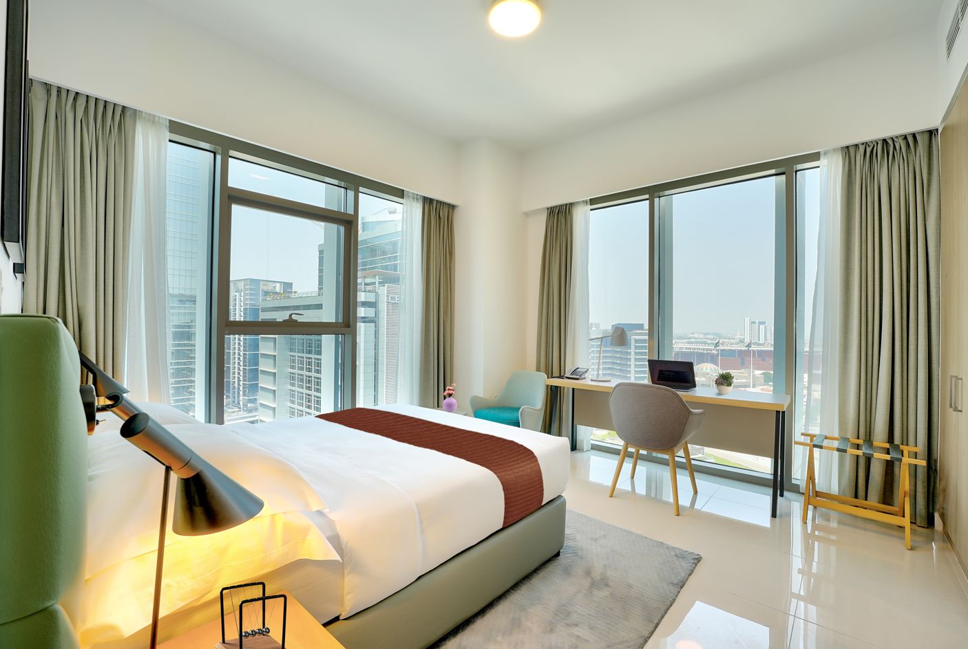 Habitación de hotel con una cama grande, un escritorio y una silla. Cuenta con ventanas amplias con cortinas.