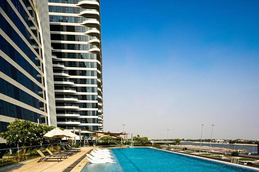 A modern hotel with a swimming pool, outdoor seating, and a view of the city.