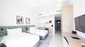 A modern hotel room with a bed, bedside tables, a desk, a TV, and a kitchenette.