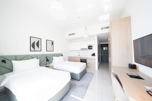 A modern hotel room with a bed, bedside tables, a desk, a TV, and a kitchenette. - Capital Suites Hotel Apartments (Abu Dhabi)