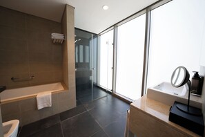 A modern bathroom with a bathtub, a sink, and a large mirror. There is a glass door leading to a shower area. - Capital Suites Hotel Apartments (Abu Dhabi)