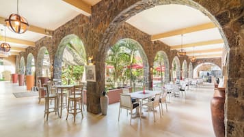 Un comedor interior con arcos de piedra, mesas y sillas.