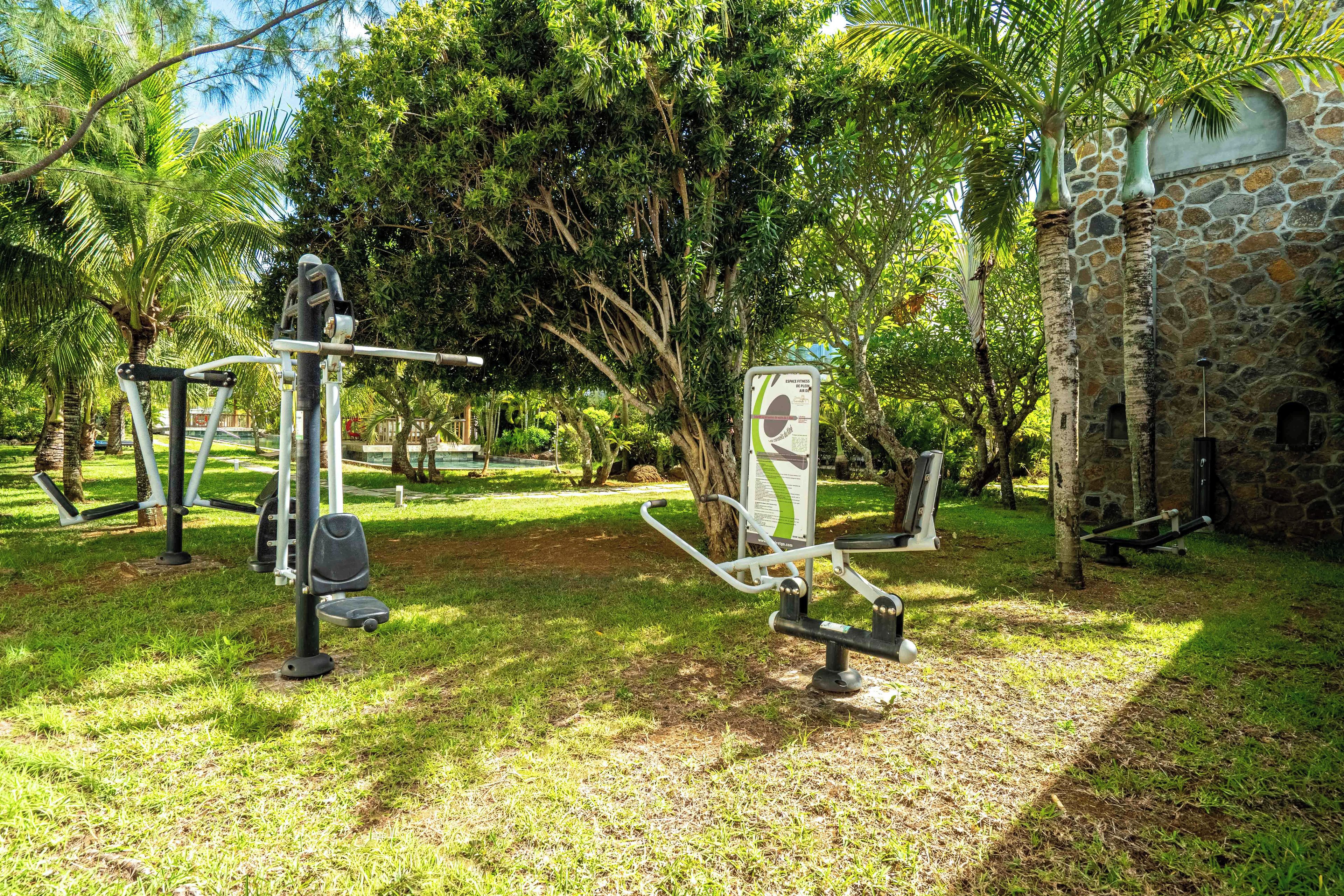 Equipos de ejercicio al aire libre, un edificio de piedra y exuberante vegetación en un parque.