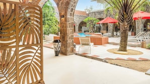 A pool area with stone arches, red umbrellas, and a palm tree.