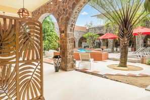 A pool area with stone arches, red umbrellas, and a palm tree.