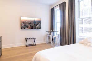 Una camera d'hotel con un letto, un tavolino con sedie, un quadro raffigurante un panorama urbano e una finestra con tende.