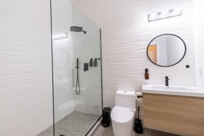 Un bagno moderno con doccia vetro, servizi igienici e lavandino con specchio.