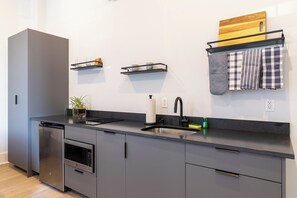 Una cucina moderna con mobili grigi, un piano di lavoro nero, forno integrato, lavandino e un ripiano in legno a parete con asciugamani da cucina.